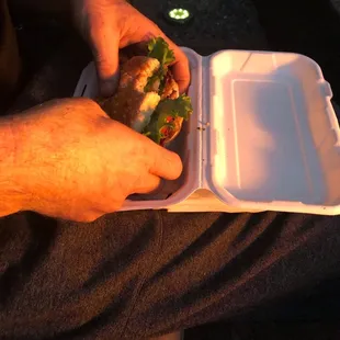 a man holding a sandwich in a styrofoam container