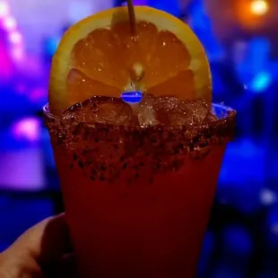 person holding a drink with a slice of orange on the rim