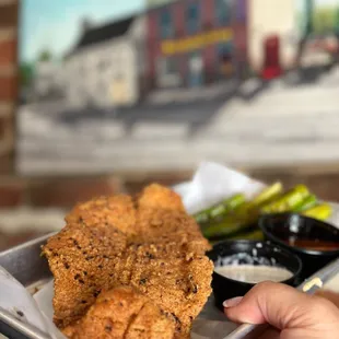 a hand holding a tray of fried chicken