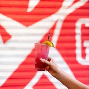a person holding a drink in front of a red wall