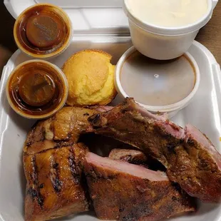 Chicken and ribs plate with beans and potato salad, corn muffin and barbecue sauce.