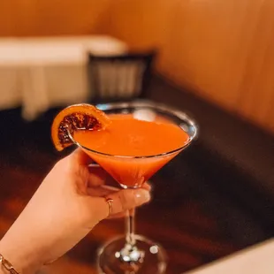 a woman holding a martini glass with a blood orange garnish