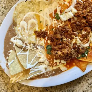 Chilaquilas. Tortilla chips with ranchero sauce, chorizo, queso fresco, onions, crema, &amp; cilantro. Comes with two eggs &amp; refried beans.