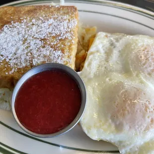 Morning Monte Cristo: French toast layered with cheese, choice protein, two eggs any style, strawberry compote, and hash browns on the side.