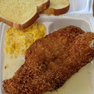 a chicken breast, scrambled eggs, and bread