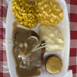 a plate of food with meat, mashed potatoes, corn and gravy
