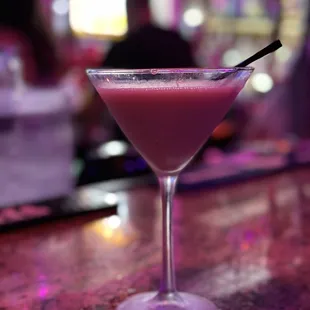 a pink drink in a martini glass on a bar