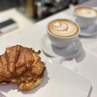 a croissant sandwich and two cups of coffee