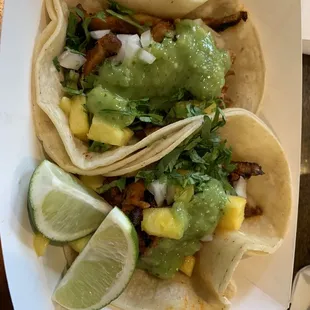 two tacos with guacamole and lime wedges
