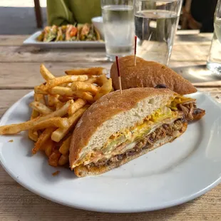 Cubano (pulled pork, ham, mustard, Swiss cheese, chipotle aioli, black beans, and pickles on a ciabatta roll) and French Fries.