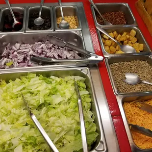 From bottom left to right: Head Lettuce, Shredded Cheese, Sunflower Seeds, Onions, Croutons, Beets, Black Olives, Peanuts, Bacon.