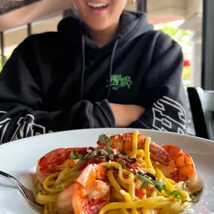 a woman sitting at a table with a plate of pasta and shrimp