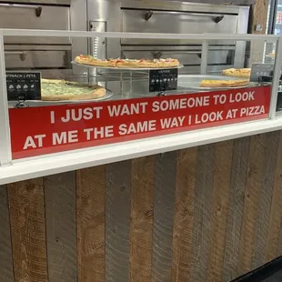 a pizza counter with a sign that says i just want someone to look at me the same way i look at pizza