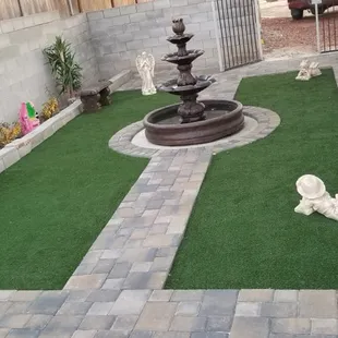 Paved walkway, fountain, stone benches and artificial grass installation.