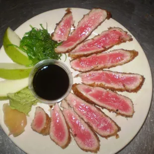 a plate of sliced steak with a dipping sauce