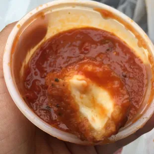 a hand holding a bowl of tomato sauce