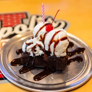 a piece of brownie with ice cream and a cherry on top