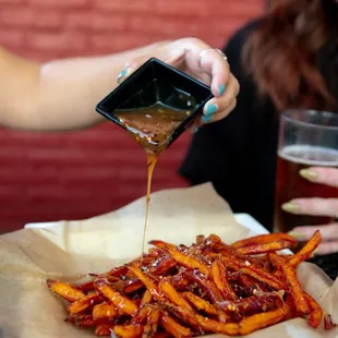 a woman pouring caramel over a plate of fries