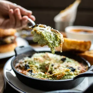 a person dipping a piece of bread into a cast iron skillet