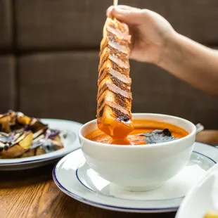 a person dipping a piece of bread into a bowl of soup