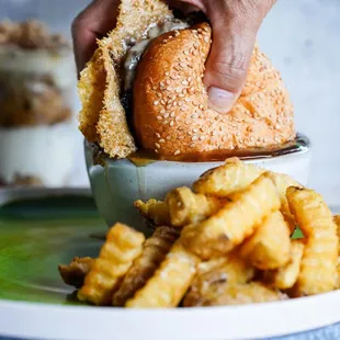a hand grabbing a sandwich from a bowl of fries