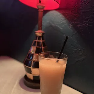 a glass of orange juice on a table next to a lamp