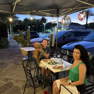two people sitting at a table with a dog