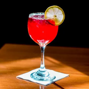 a red cocktail with a slice of lemon on the rim