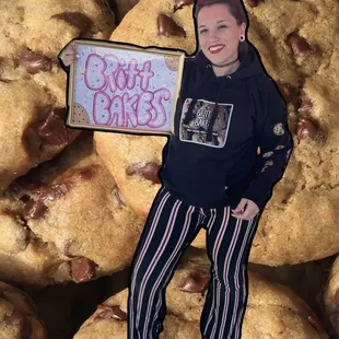 a woman holding a sign in front of a pile of chocolate chip cookies