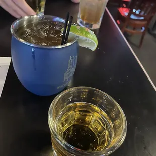 a drink in a blue mug and a glass with a lime wedge