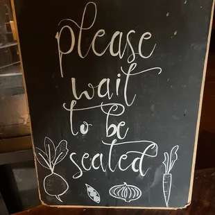 a sign that says please wait to be seated