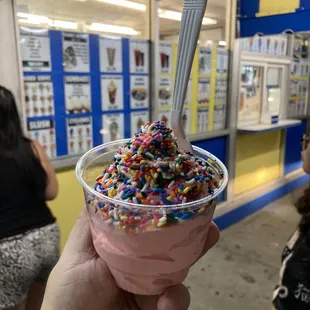 a hand holding a cup of ice cream with sprinkles