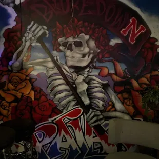a skeleton with a scyther in front of a mural