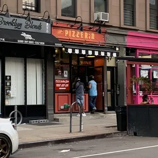 people walking in front of a pizza shop