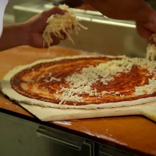 a person putting cheese on top of a pizza