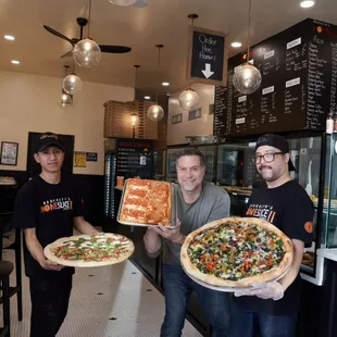 One of the partners and staff holding some of our selection of pizza