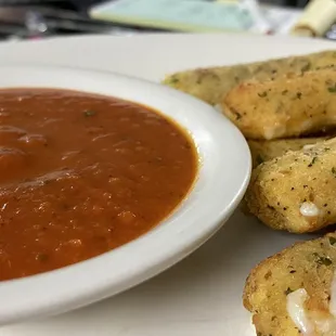 a bowl of tomato sauce and a plate of breadsticks