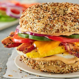 a bagel sandwich with bacon, cheese, peppers, and onions