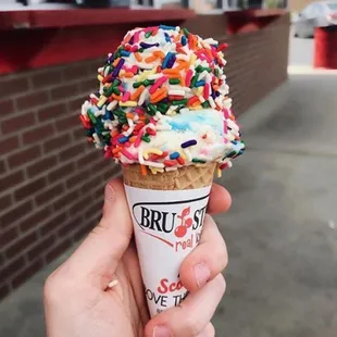 a hand holding an ice cream cone with sprinkles