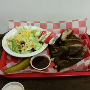 a plate of ribs, salad and pickle