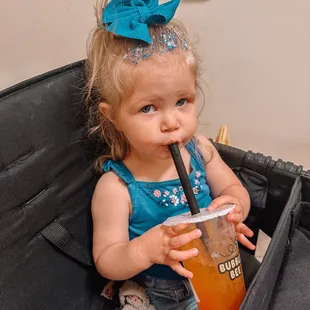 a little girl sitting in a suitcase with a drink
