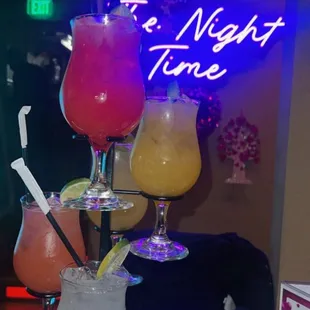 three cocktails on a table in front of a neon sign