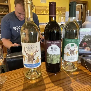 a man at a bar with three bottles of wine