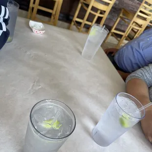 a woman sitting at a table with a glass of water and a glass of lemonade