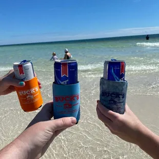 two people holding cans of beer on the beach