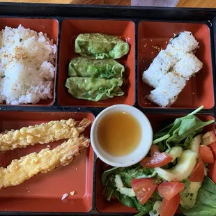 Bento box with rice, vegetable gyoza, California roll, tempura shrimp and salad.