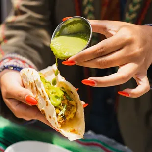 a person pouring guacamole on a tortilla