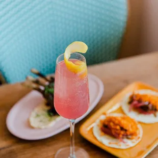 a pink cocktail with a slice of lemon