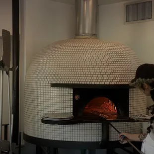 a woman putting a pizza in a brick oven