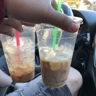 a hand holding two cups of iced coffee